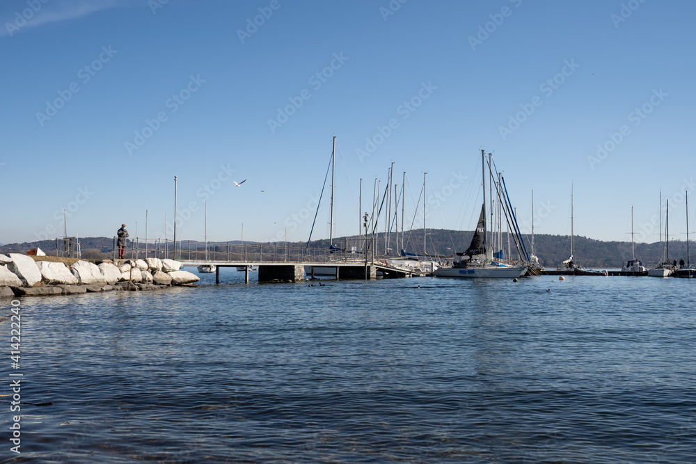 The quay with boats moored at Lake Maggiore, Arona, Italy. A standing man looks at the phone far away