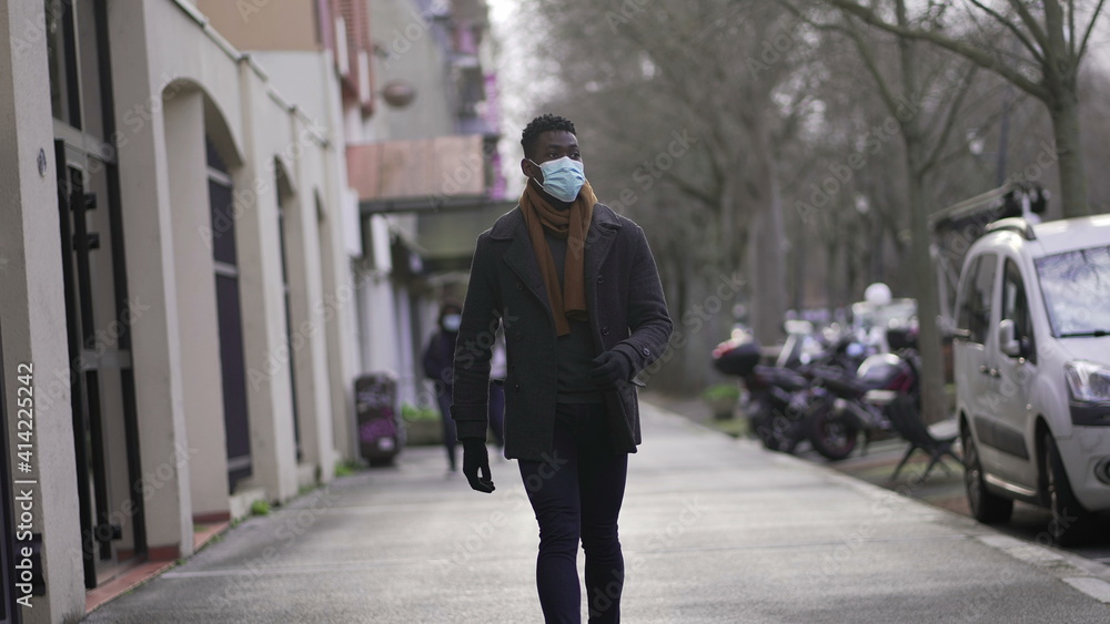 Black man wearing covid face mask walking outside in city downtown