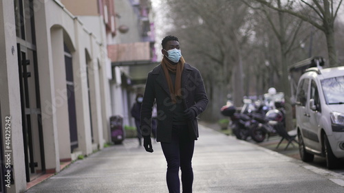 Black man wearing covid face mask walking outside in city downtown