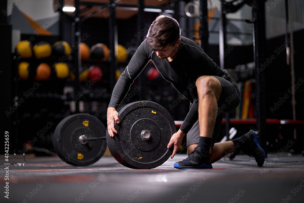 Athlete male adding weight plates on his barbell, young caucasian fit guy preparing for weightlifting workout at gym alone. bodybuilding concept Athlete male adding weight plates on his barbell, young caucasian fit guy preparing for weightlifting workout at gym alone. bodybuilding concept