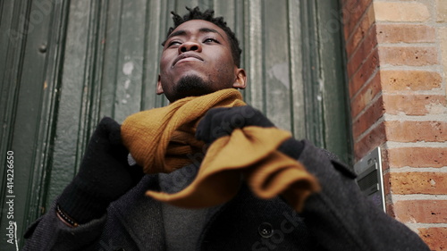 Black steps out front home door putting scarf preparing for the cold