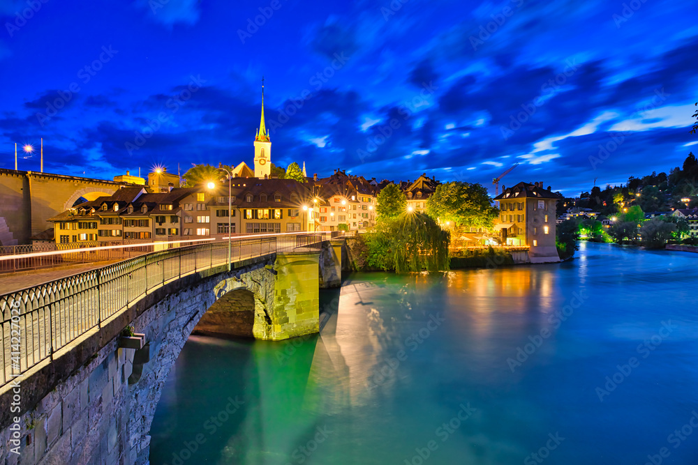 Obraz premium Scenic view of Untertorbrucke bridge in Bern old town with view of Nydeggkirche church. Capital of Switzerland, historic center. Urban cityscape at evening reflecting in the Aare river.