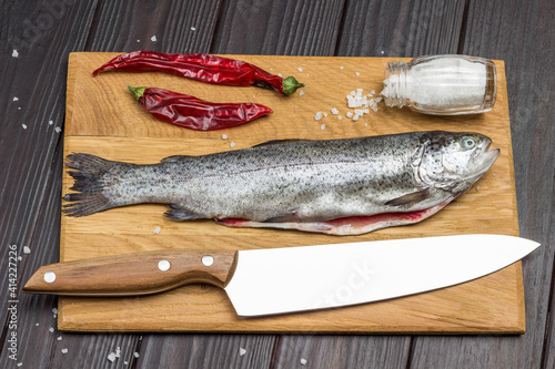 Peeled fish trout, red paper, salt and knife on cutting board