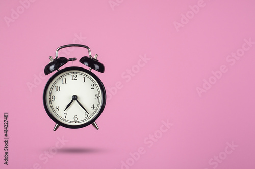 Black alarm clock on a pink background. Creative composition.