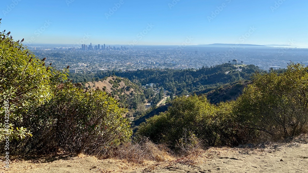 Wide view of Los Angeles county, with Downtown city skyline and Griffith Park observatory seen from hiking trails, cloudless day with blue skies