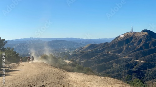 Photo Horse riders kicking up dust on trail through Griffith Park with Hollywood sign