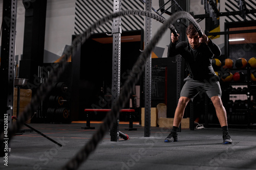 Athlete man training with rope, cross fit battle ropes exercise alone, intense workout indoors, in modern gym. Sport motivation concept. Copy space. © alfa27