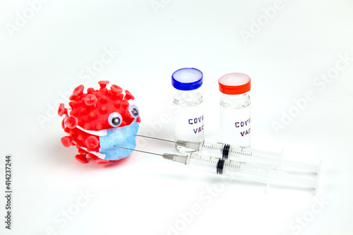 A plastic red ball with protruding umbrellas bulging eyes a blue mask similar to covid pricked with medical syringes and vials with the text covid-19 vaccine on a white background. Medicine viral infe photo