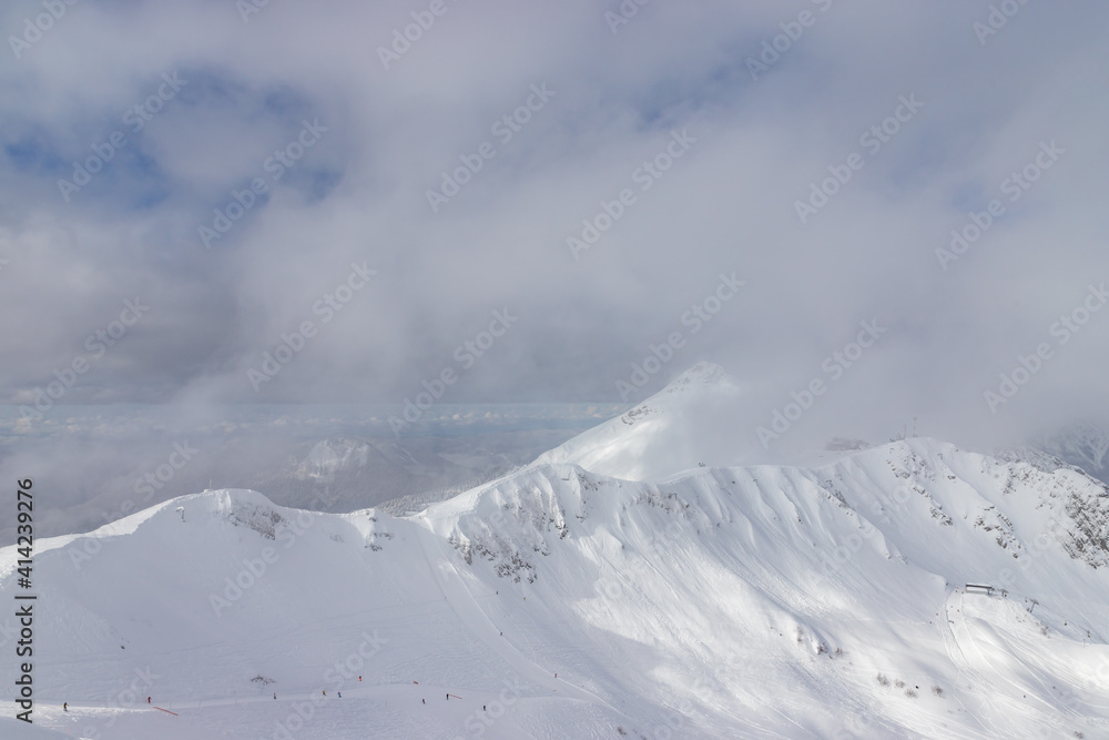 Snow-covered mountains and ski slopes with clouds on background. Ski resort Roza Khutor. Sochi. Russia.
