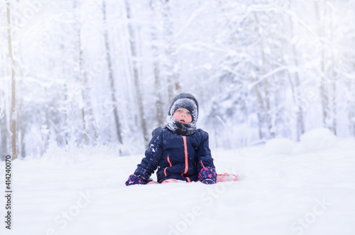 little girl sitting on the snow in the winter forest