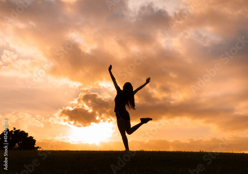 Happy young female feeling free in nature with arms raised up to the sunset sky. 