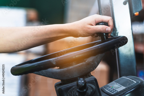 Selective focus shot of man's hand on the steering wheel of a forklift truck in a factory