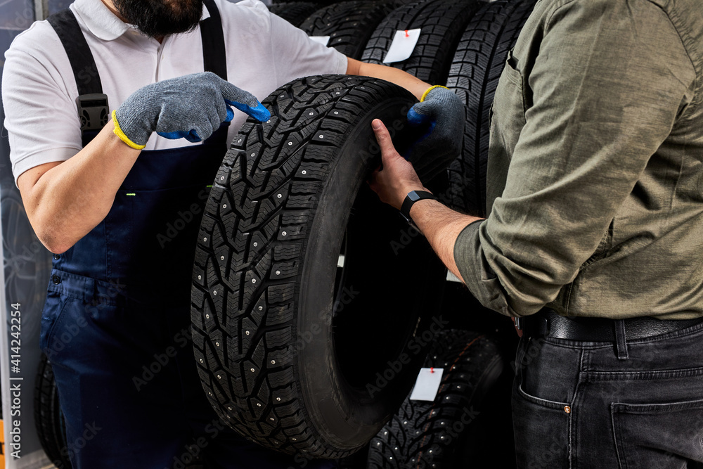 Fototapeta premium salesman of tires talking about characteristic of product to customer came to look at assortment represented in auto service shop