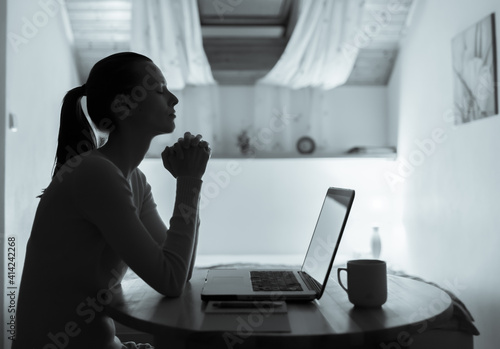 Fotografie Young woman saying a prayer working on her office computer.