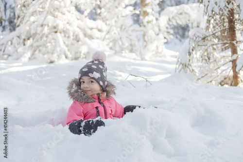 Little girl sitting in snow, have fun, enjoy wintertime.