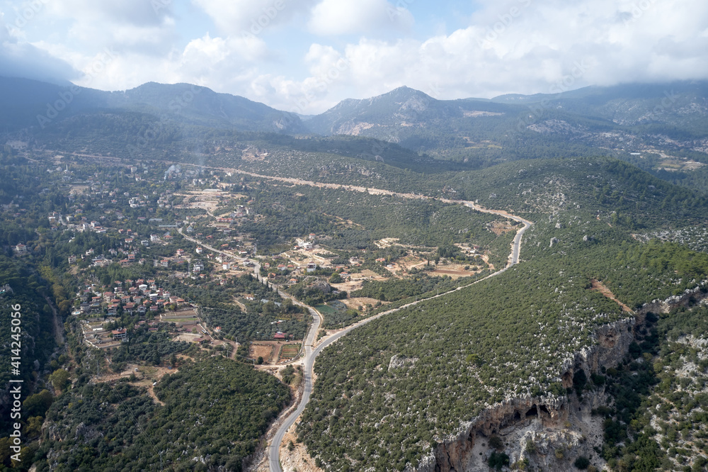 Top view to the forested valley on a cloudy day. Aerial view of picturesque mountain valley with village and road.