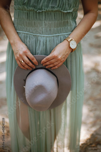 the body of a girl in a dress who holds a hat in her hands. golden watch golden rings. female hands holding grey hat 
