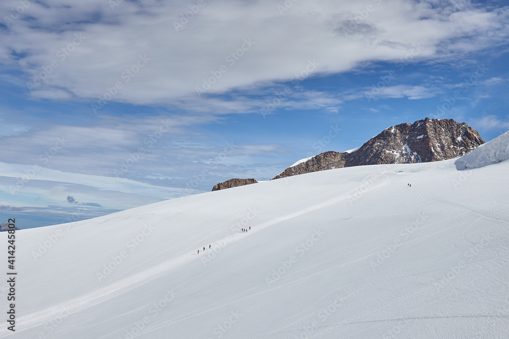 Monte Rosa Massive, Italian Alps - the glacier surrounded by summits with altitude over 4000 m, people trekking in climbing party in the distance Monte Rosa Massive, Italian Alps - the glacier surrounded by summits with altitude over 4000 m, people trekking in climbing party in the distance