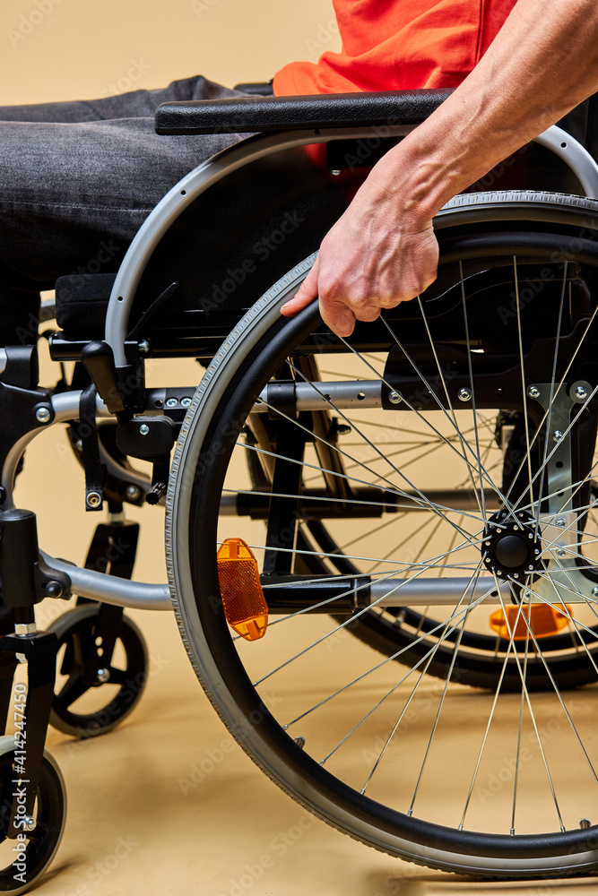 disabled handicapped man touching wheels and sitting in profile while moving ahead isolated in studio. close-up photo of wheelchair and hands
