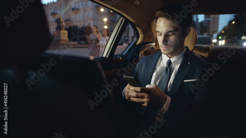 Businessman writing message on smartphone in car. Man typing text on mobile