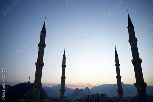 Four minarets against a sunset sky. Silhouette of mountains in the background.