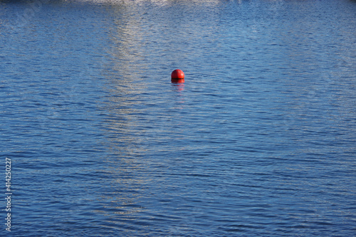 View of the blue pacific ocean water in a southern California harbor with some reflections and a red buoy