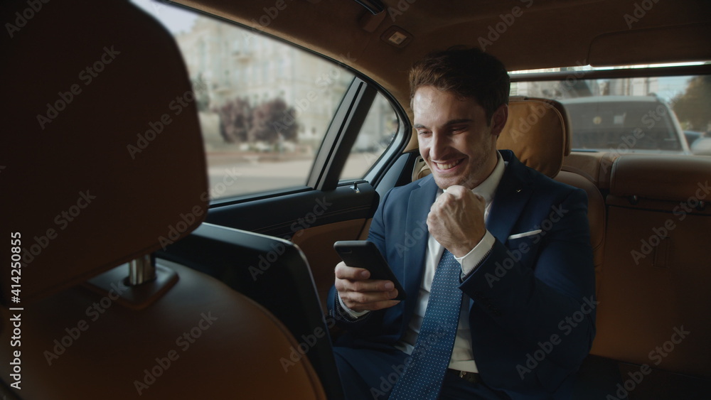Surprised businessman getting good news on smartphone in interior of modern car.