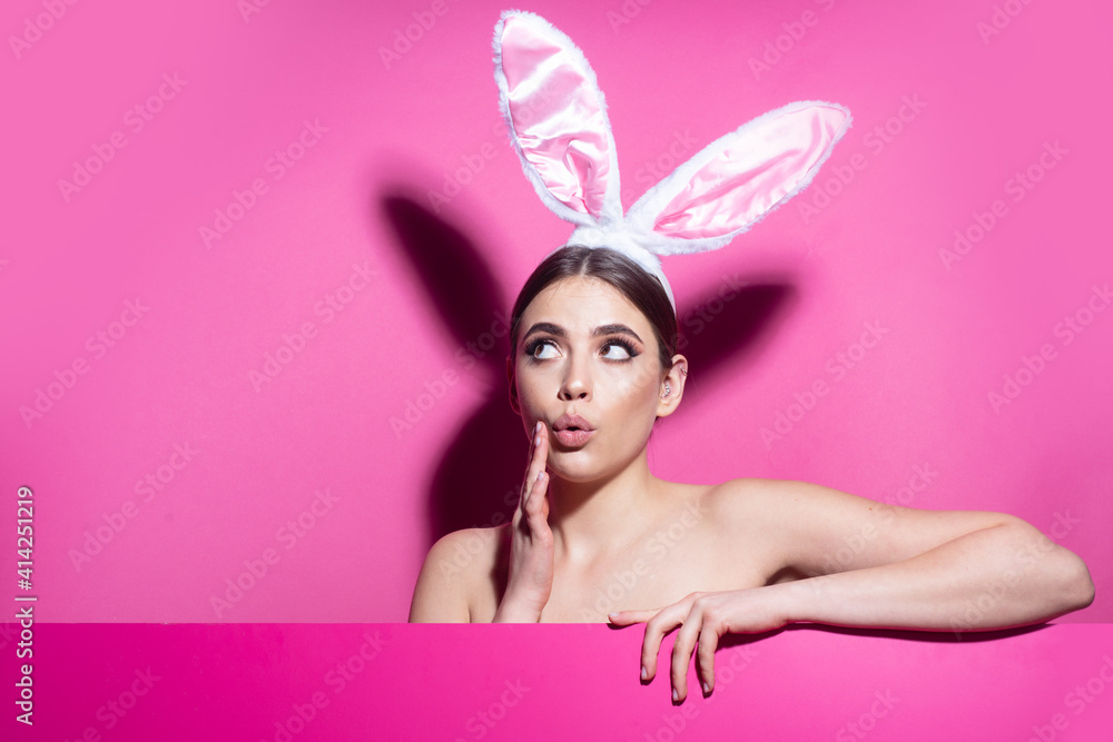 Surprised young woman wearing rabbit ears isolated on pink.