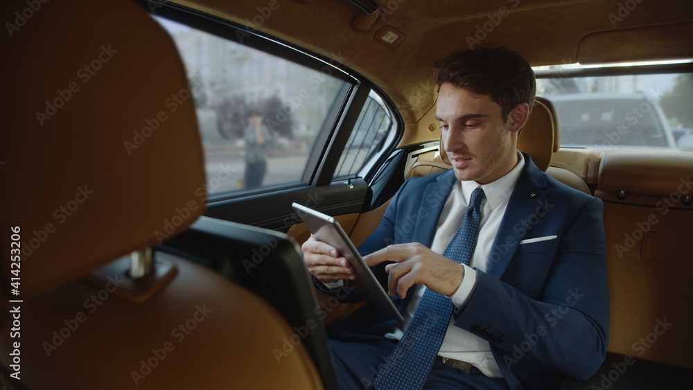 Smiling male professional reading good news on tablet computer in automobile.