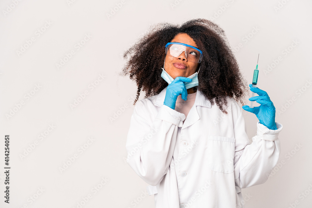 Young african american curly doctor woman holding a syringe looking sideways with doubtful and skeptical expression. Young african american curly doctor woman holding a syringe looking sideways with doubtful and skeptical expression.