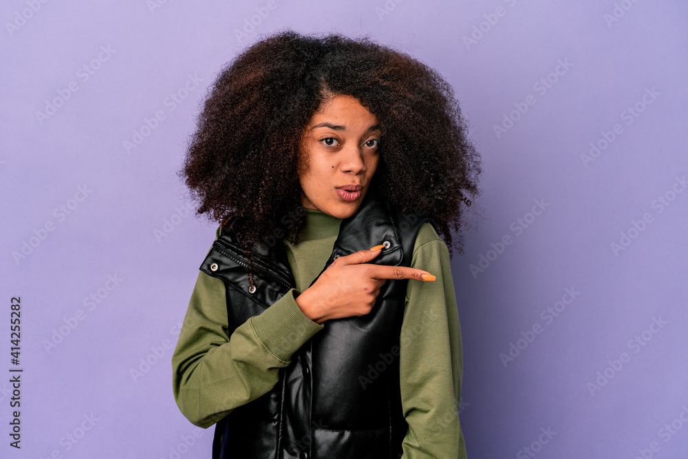 Young african american curly woman isolated on purple background smiling and pointing aside, showing something at blank space. Young african american curly woman isolated on purple background smiling and pointing aside, showing something at blank space.