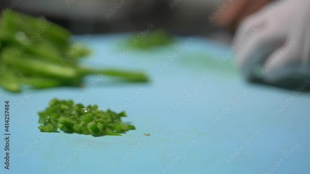 Gloved hands slowly chopping pepper slices on blue cutting board Gloved hands slowly chopping pepper slices on blue cutting board