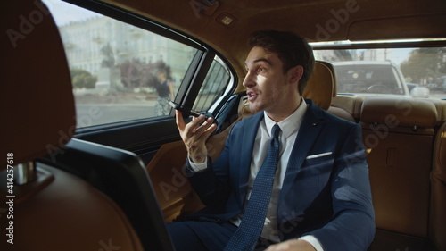 Happy businessman sharing joy in voice message to mobile phone in business car. © stockbusters