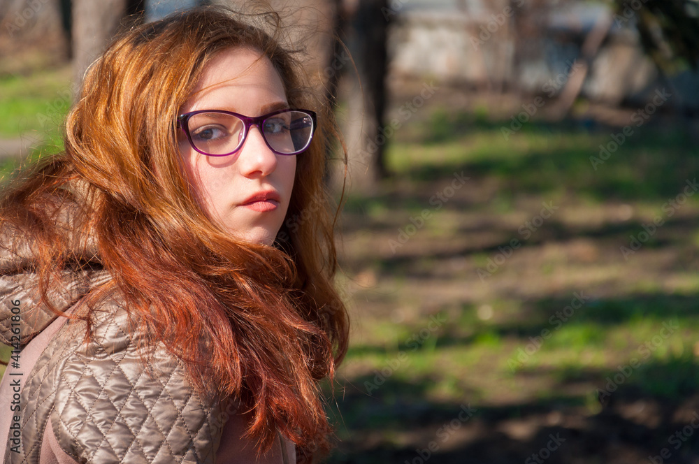 Portrait redhead girl outdoors in autumn on a background of trees and shrubs Portrait redhead girl outdoors in autumn on a background of trees and shrubs