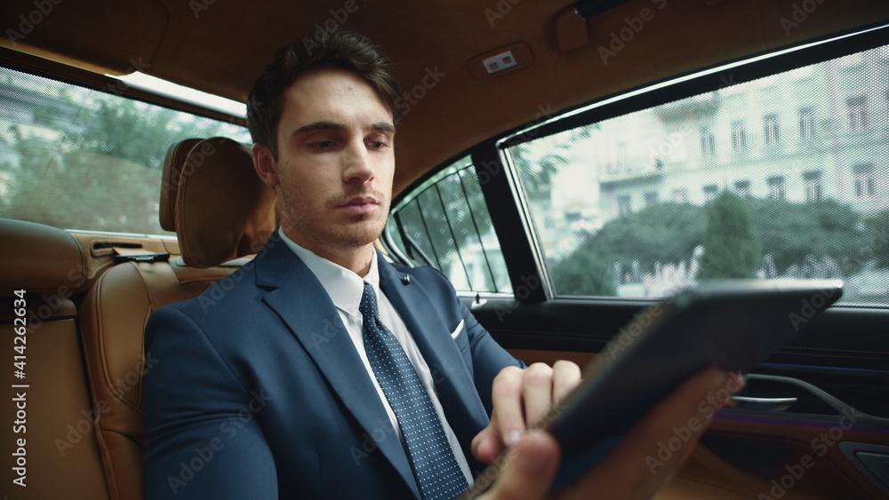 Portrait of focused business man working on tablet computer in business car.