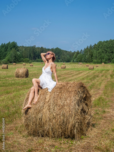 Girl in a field by a bale of hay on a summer day