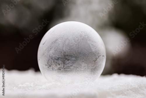 One frozen soap bubble on white snow with dark background
