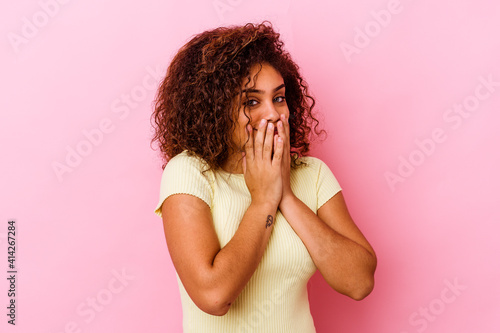 Young african american woman isolated on pink background laughing about something, covering mouth with hands. © Asier