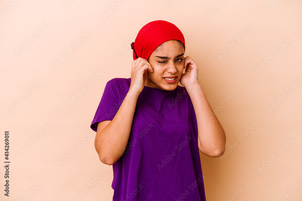 Young african american woman isolated on beige background covering ears with fingers, stressed and desperate by a loudly ambient. Young african american woman isolated on beige background covering ears with fingers, stressed and desperate by a loudly ambient.