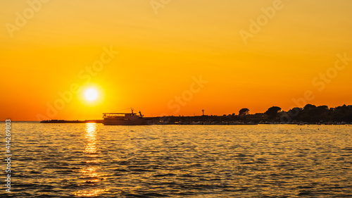 Amazing sunset with defined Sun and reflection on water. Silhouettes of boats and cruise ship moored at marina on Adriatic Sea, Zaton, Croatia © Dawid