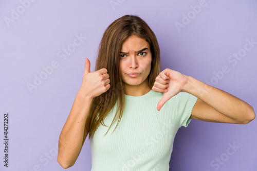 Young skinny caucasian girl teenager on purple background showing thumbs up and thumbs down, difficult choose concept