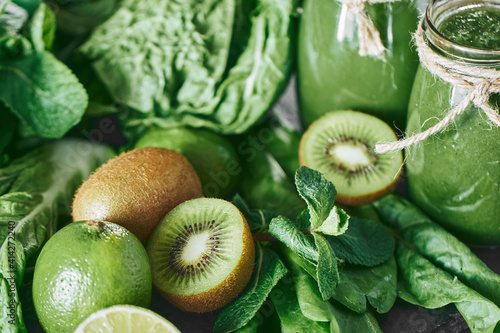 Blended green smoothie with ingredients on the stone board, wooden table selective focus