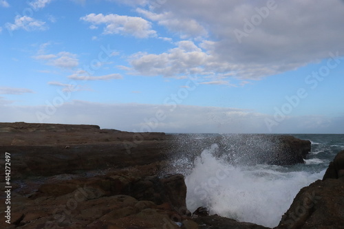 Sea waves impacts on this rock platform down below from the Norah head lighthouse in Central Coast Australia. Blue and white sky formations in the horizon.