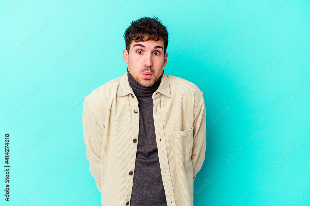 Young caucasian man isolated on blue background shrugs shoulders and open eyes confused. Young caucasian man isolated on blue background shrugs shoulders and open eyes confused.