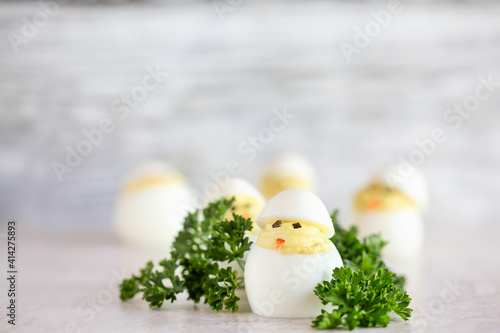 Deviled eggs for Easter decorated as cute little chicks hatching from eggs with carrot beak and seaweed eyes. Extreme shallow depth of field with blurred background and room for copy space. 