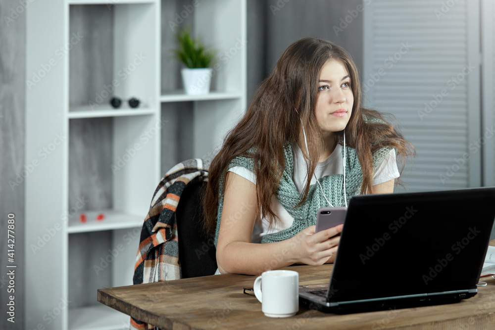 A focused student girl is preparing for a test exam doing homework at home while sitting at a desk with a laptop. The concept of self-education, distance learning. A focused student girl is preparing for a test exam doing homework at home while sitting at a desk with a laptop. The concept of self-education, distance learning.