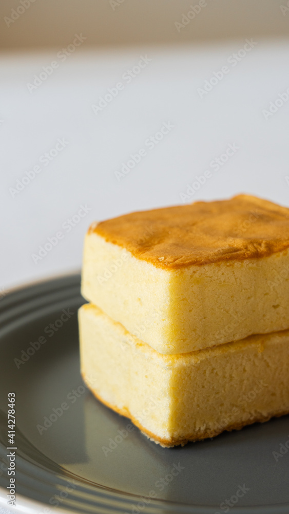 Square fluffy egg sponge cake on a black plate, breakfast pastry, vertical image