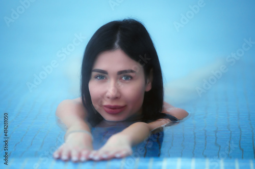 Beauty brunette woman lies and relaxes in mineral water in pool at spa, hot springs resorts. Model looking at camera. Soft selective focus on eyes. photo