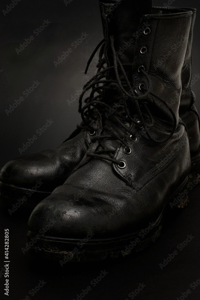 A pair of old, worn, black leather army boots, with traces of dirt and mud on them.