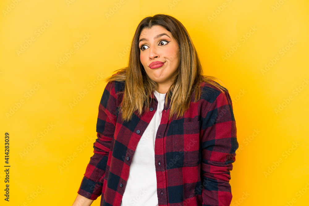 Young indian woman isolated on yellow background shrugs shoulders and open eyes confused. Young indian woman isolated on yellow background shrugs shoulders and open eyes confused.